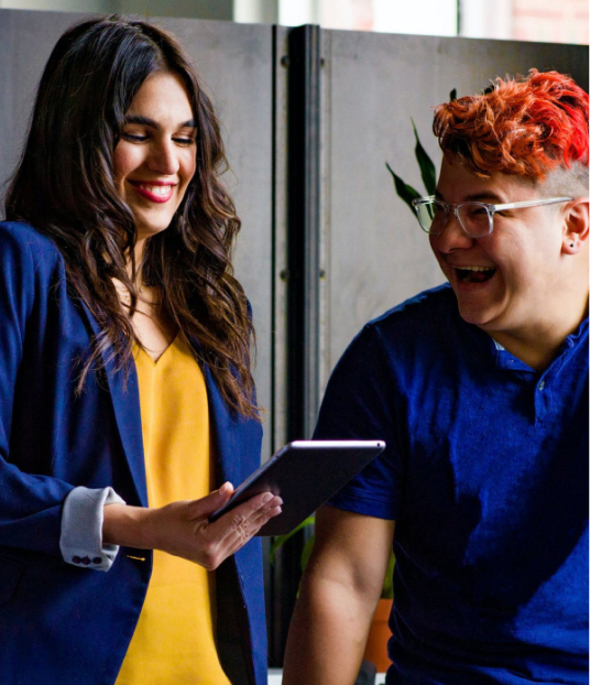 Two members of a startup team smiling while reviewing work on a tablet